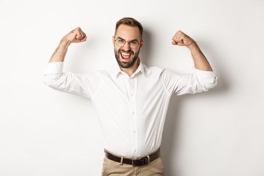 Successful manager flex biceps, showing muscles and looking confident, standing over white background