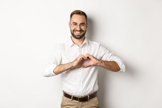 Handsome manage showing heart sign and smiling, I love you gesture, standing over white background