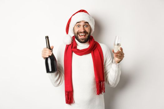 Christmas party and holidays concept. Happy bearded male model in Santa hat and red scarf, celebrating xmas, partying with glass of Champgne, white background