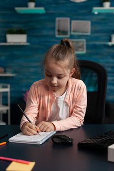 Little schoolchild sitting at desk table in living room writing mathematics exercices
