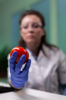 Closeup of scientist reseacher woman analyzing tomato injected with pesticides during scientific agriculture experiment. Biochemist scientist doctor working in microbiology hospital laboratory
