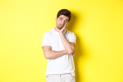 Bored and gloomy guy looking up, imaging things, standing over yellow background