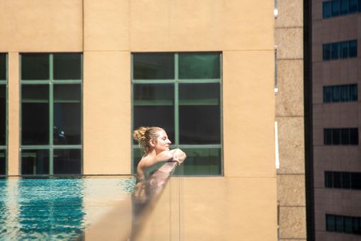 young caucasian woman relaxing in a pool on the roof of a skyscraper in a metropolis under the sun