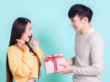 Young man giving a surprise gift to woman.Isolated on blue background.