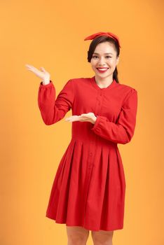 Beautiful young asian woman presenting your very exciting product. Isolated on yellow background.