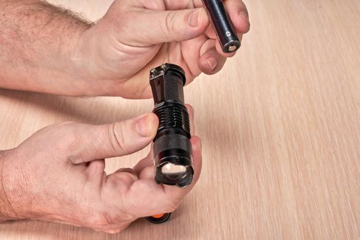 Hands hold a small black flashlight and replace the battery in it