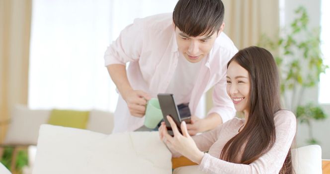 Happy young couple sitting on  couch and  looking at mobile phone