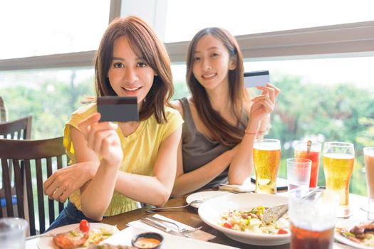Happy young women showing the credit card  in restaurant