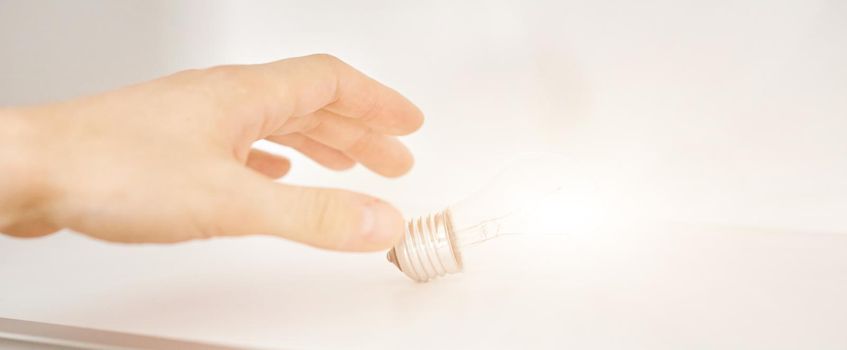 hand reaches for a glowing light bulb on a white shelf. The concept of aspiration behind the idea