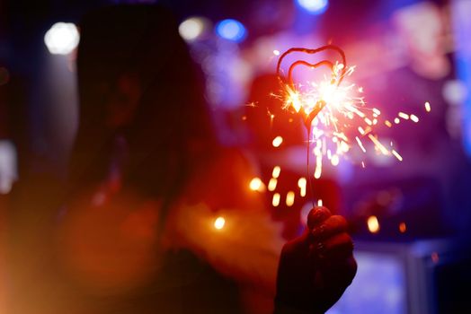 Girl holding burning sparkler in heart shape