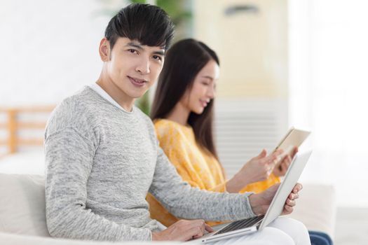 Young couple sitting and using laptop and tablet together in the living room.