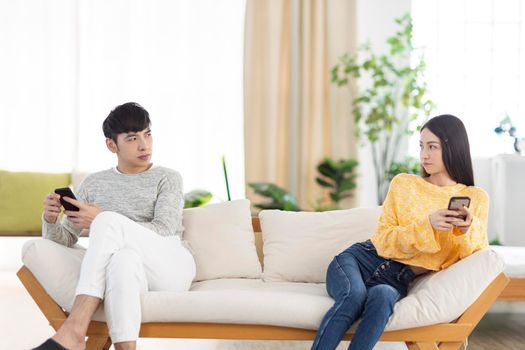 Young couple being in quarrel and not talking.Sitting in living room.Using smartphone.