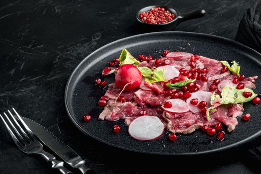 Delicatessen appetizer of fresh marbled meat - beef carpaccio, with Radish and garnet, on plate, on black stone background, with copy space for text