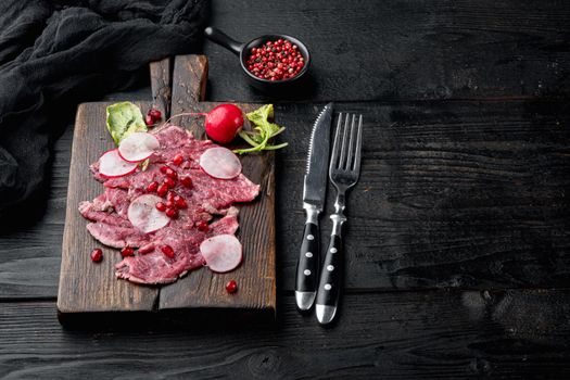 Delicatessen appetizer of fresh marbled meat - beef carpaccio, with Radish and garnet, on wooden serving board, on black wooden table background, with copy space for text