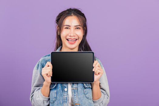 Portrait of Asian beautiful young woman confident smiling show blank screen with tablet computer, Happy lifestyle female teen showing digital tablet pc, studio shot isolated on purple background
