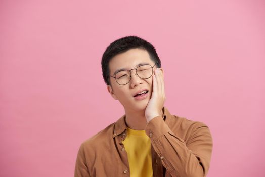 A young and handsome Asian man uses his hand to touch and hold his mouth with painful and suffer face from toothache.