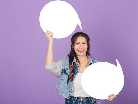 Happy Asian beautiful young woman smiling excited wear denims hold empty speech bubble sign, Portrait female posing show up for your idea looking at camera, studio shot isolated on purple background