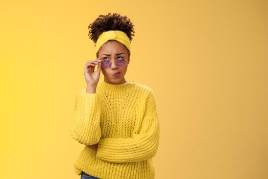 Perplexed unsure stylish african-american female creative designer in headband sweater sunglasses smirking folding lips tube uncertain have doubts frowning look up thoughtful cannot decide
