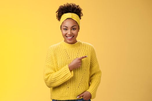 Friendly ougoing relaxed african-american woman casually pointing right during conversation discussing recent new cafe open awesome discounts promos standing happily yellow background