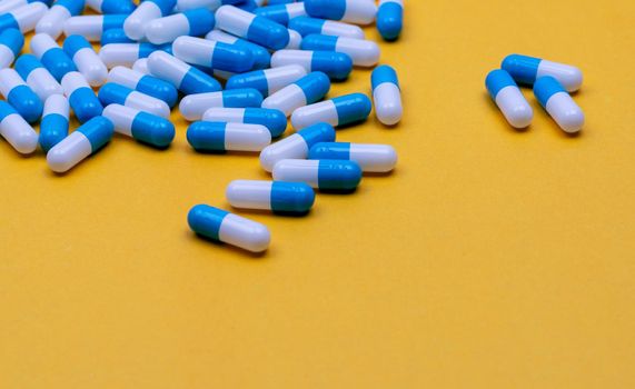 Blue and white antibiotic capsule pills spread on yellow background. Antibiotic drug resistance. Antimicrobial drug. Pharmaceutical industry. Pharmaceutical products for pharmacy shop and hospital.