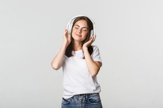 Dreamy beautiful girl enjoying listening music in wireless headphones, smiling happy