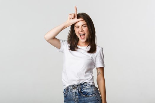 Sassy good-looking girl smiling and mocking person, showing loser gesture on forehead
