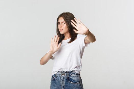 Scared and insecure cute girl raising hands in stop gesture, defending herself