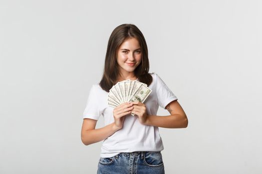 Greedy smiling girl looking cunning and holding money, standing white background