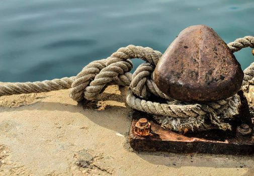 Rusty mooring bollard with tied rope in the port