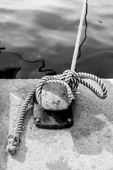 Rusty mooring bollard with tied rope in the port