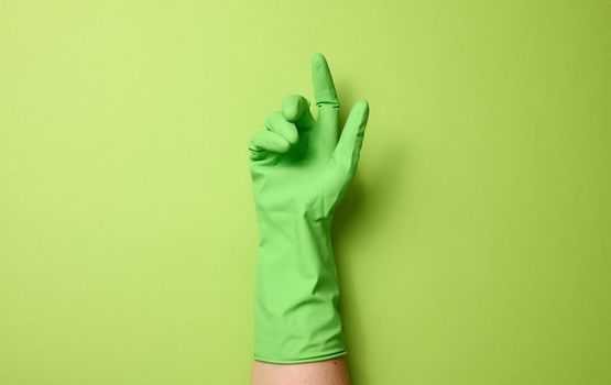 hand in a rubber green glove for cleaning on a green background, part of the body is raised up