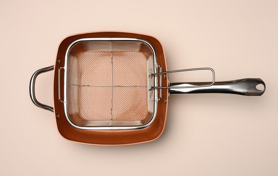 empty copper deep frying pan with grill grate on beige background. View from above