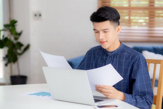 Young asian business man looking document data graph and chart paper, marketing and investment, report of statistics profit for financial, economic and growth of finance, management and planning.