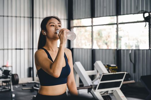 Asian young woman drinking water after workout in gym, healty and sport concept.