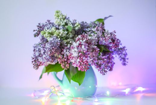 Beautiful bouquet of fragrant purple flowers in blue ceramics vase on light background. Syringa vulgaris or lilacs plant.