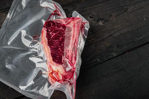 Dry aged beef marbled meat, raw fresh club beefsteak in plastic package, on black wooden table background, with copy space for text