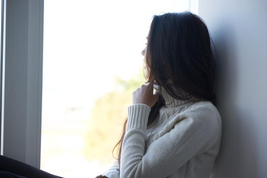 sad woman near the window in a white sweater loneliness