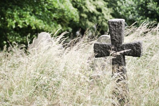 Old stone cemetery cross in tall grass with differential focus