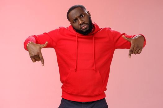 Cheeky stylish good-looking black bearded guy look cool tilting head bossy confident frowning seriously pointing down showing awesome place hang out homies, standing pink background