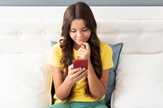 Happy girl child smile chatting on mobile phone while sitting on bed, chat
