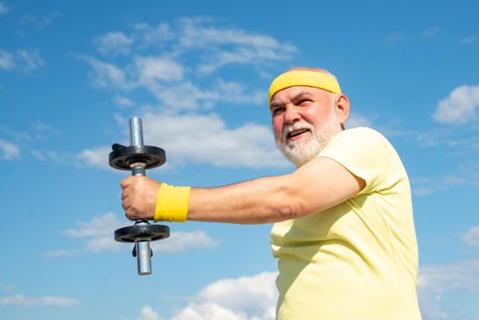 Grandfather sportsman portrait on blue sky backgrounds. Portrait of healthy senior. Senior man in his seventies training and lifting weigh.