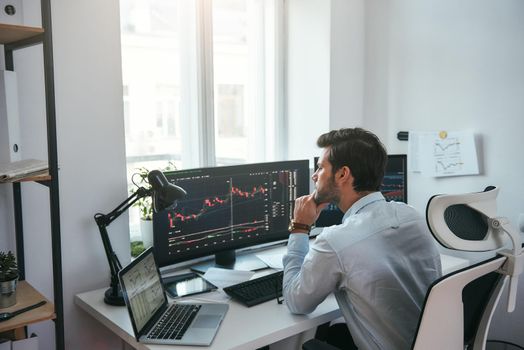Trading on world markets. Young stock market broker analyzing data and graphs on multiple computer screens while sitting in modern office