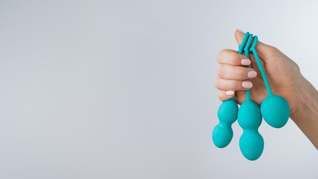 A faceless woman demonstrates a set of mint-colored vaginal balls. Girl holding a kegel trainer for training pelvic floor muscles on a white background.