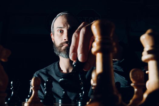 Young adult handsome man playing chess in dark with side lit