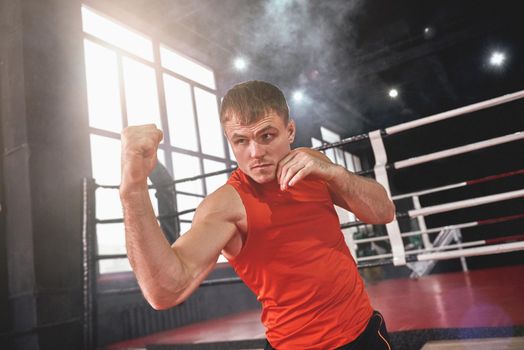 Training to become the best. Focused muscular athlete in sports clothing boxing with shadow while standing opposite boxing ring