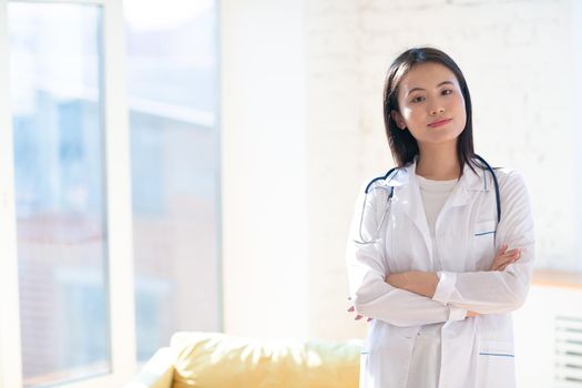Asian positive doctor woman in white medical gown with stethoscope against clinic interior indoor background portrait