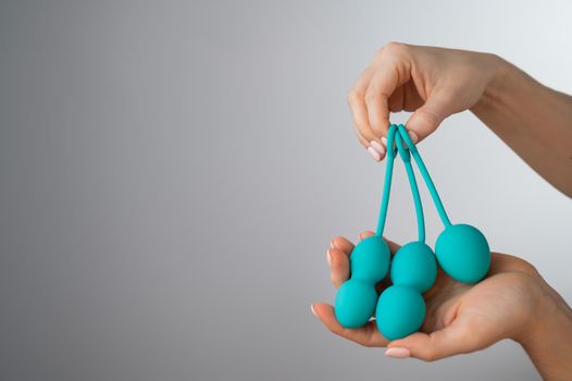 A faceless woman demonstrates a set of mint-colored vaginal balls. Girl holding a kegel trainer for training pelvic floor muscles on a white background.