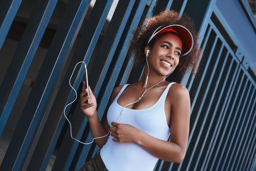 Young woman in tennis visor and earphones free style on the stre