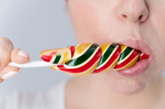 Close-up portrait of a woman sucking a long lollipop against a white background. Blowjob simulation