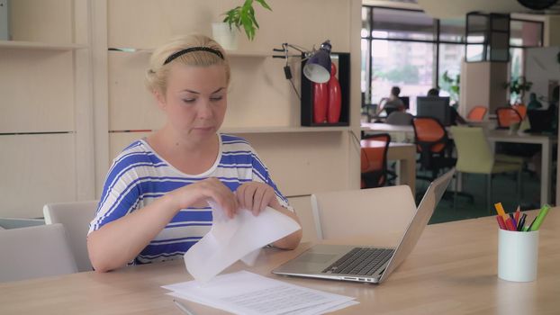 Blonde adult worker writing report and tear paper documents